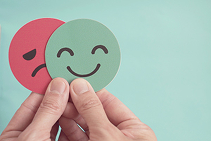 A person's hands holding two cardboard circles - one with a sad face and one with a happy face